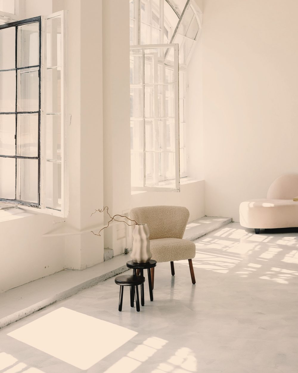 A bright, pale room with tall arched windows, an armchair, and sunlight on the floor.