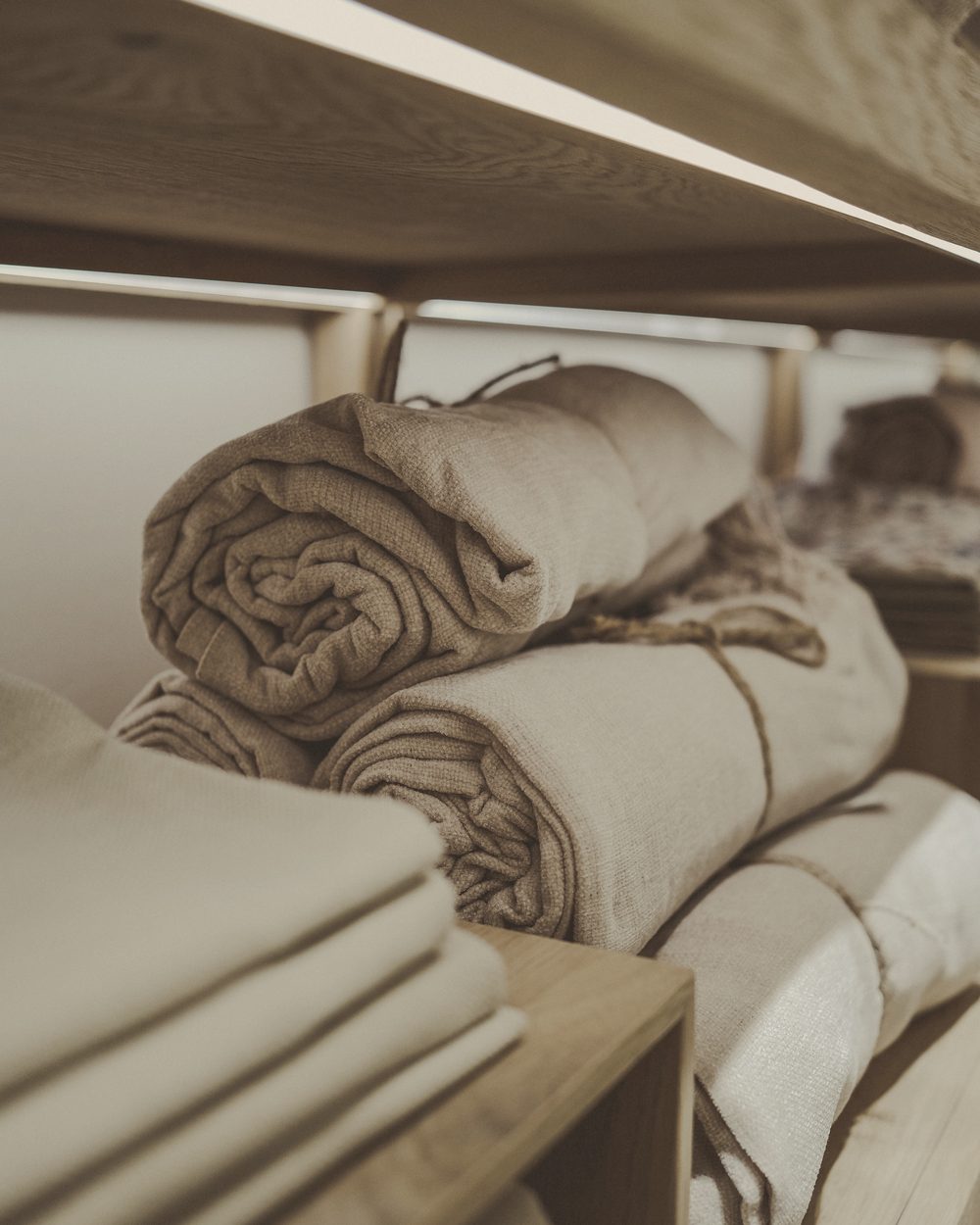 Rolled and folded linen towels on wooden shelves, from the same shoot as the hero.