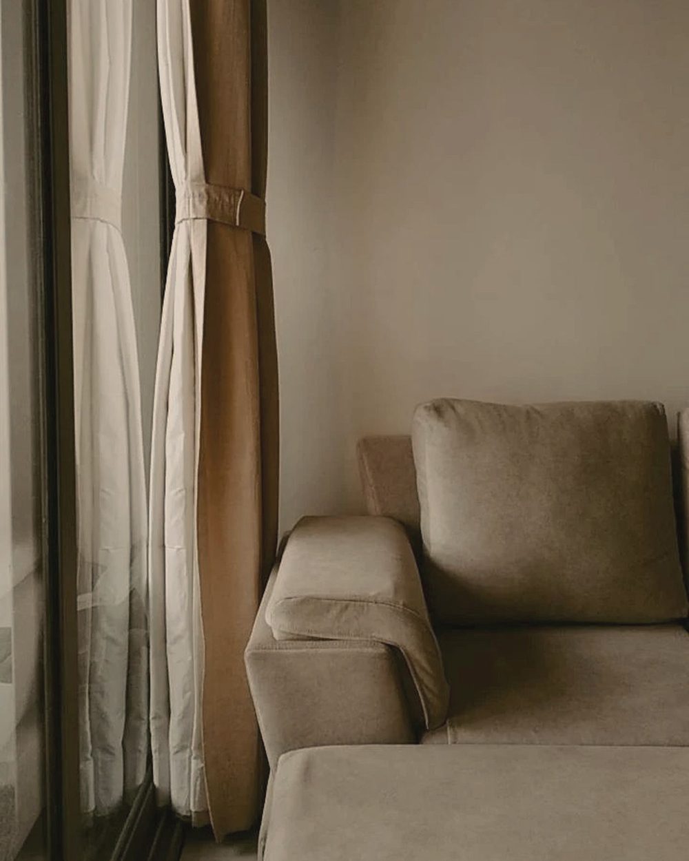 A beige sofa beside sheer and linen curtains in soft light.