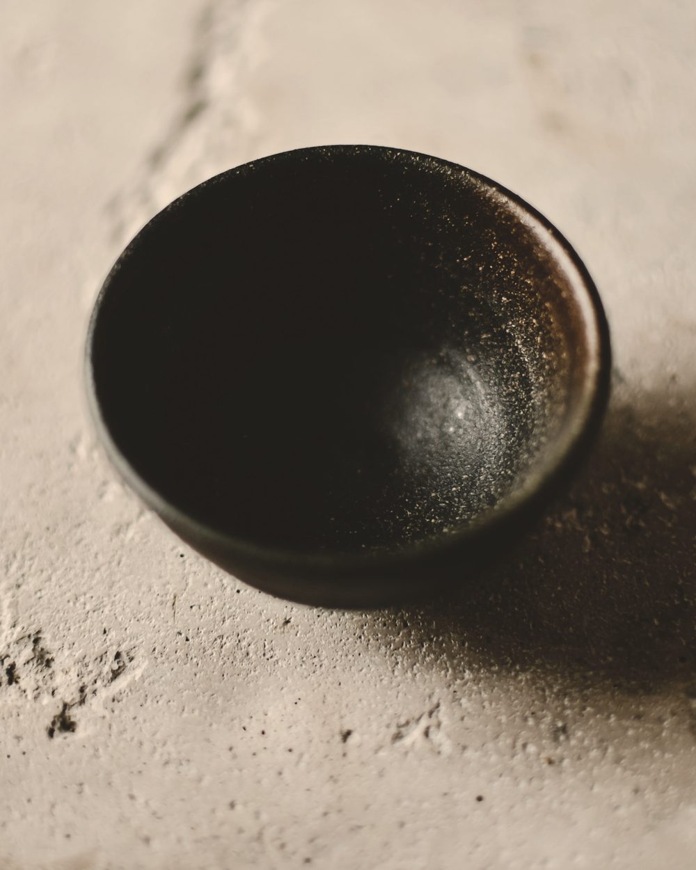 A dark glazed bowl on a pale, textured stone surface.