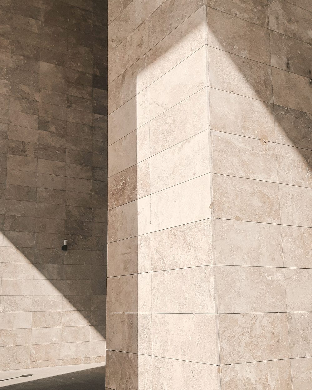 A stone-clad column and wall in soft, angled daylight.